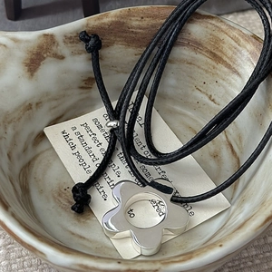 Minimalist S925 silver flower pendant on a black cord necklace in a ceramic bowl