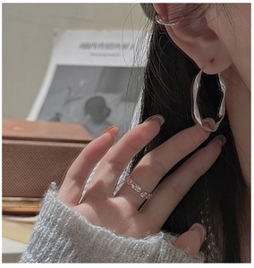 Macro shot of S925 sterling silver wavy hoop earrings and lava texture ring on model