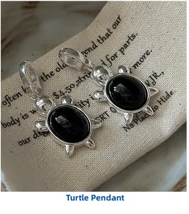 Gros plan de pendentifs tortue en argent avec pierres noires sur un sac en tissu