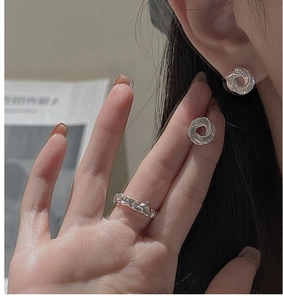 Detail of silver 3D spiral twist earrings and hammered ring on model with paper backdrop