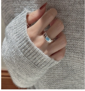 Detail of S925 silver ring with oval turquoise stone worn on hand against knitwear