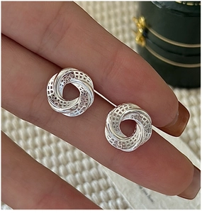 Macro shot of silver knot earrings with intricate hollow mesh texture and 3D geometric design