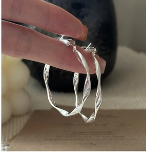 Detail of large twisted wave silver hoop earrings with polished metal finish
