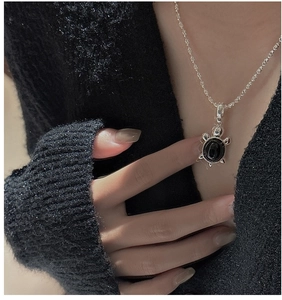Détail du collier pendentif tortue en argent avec perle noire porté par le modèle