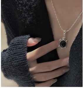 Gros plan du collier pendentif tortue avec pierre noire sur un pull en maille noir