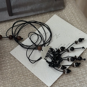 Collier artisanal de style ethnique avec pompon argenté et perles noires sur fond beige