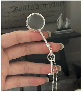 Macro shot of silver magnifying glass pendant with key handle on a delicate chain