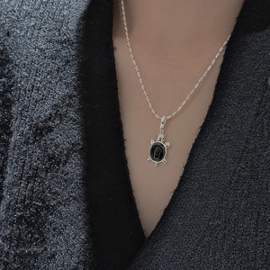 Pendentif tortue en argent S925 avec pierre noire sur fond de costume élégant noir