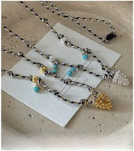 Vue détaillée du pendentif pomme de pin sur corde tressée avec perles bleues