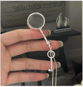 Detailed view of silver magnifying glass and vintage key pendant on a sweater chain