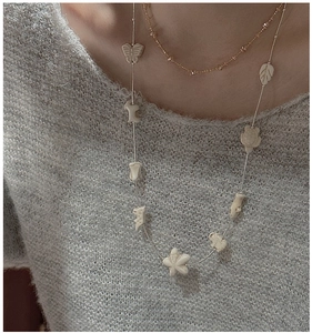 Detail of S925 silver long necklace with white animal charms on a grey knit sweater