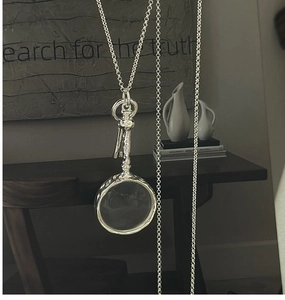 Close-up of vintage S925 silver magnifying glass pendant with key charm on long chain