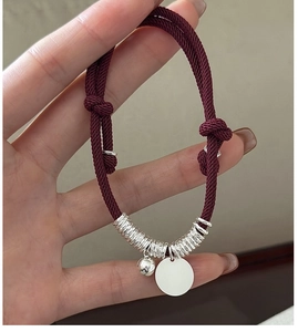 Detail of red braided rope bracelet with S925 silver charms and adjustable sliding knot