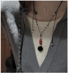 Detail of layered S925 silver necklaces with red agate pendant on a grey sweater