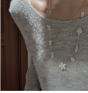 Detail of S925 silver long sweater chain with white ceramic charms on a grey knit sweater