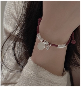 Close-up of a burgundy woven cord bracelet with silver charms on a female wrist