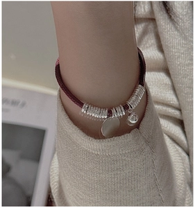 Detail of red braided rope bracelet with silver charms worn with a knit sweater