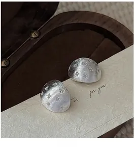 Macro shot of silver hexagram stud earrings with a brushed texture on a wood jewelry box