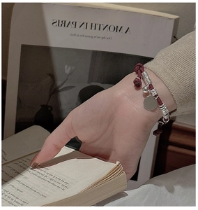 Detail of red braided rope bracelet with S925 silver charms worn against book background