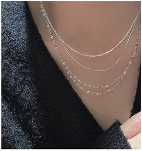 Detail view of layered S925 sterling silver necklaces on a model with black knit background