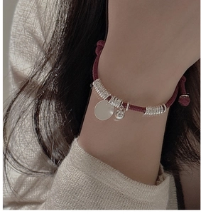 Detail of red woven cord bracelet with silver charms worn on model's wrist