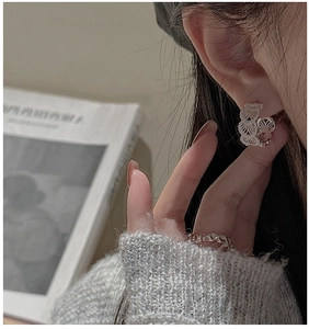 Detail of silver S925 hollow fan earrings and textured ring on model