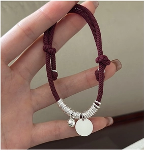 Detailed shot of red woven bracelet with silver beads and round charm on hand