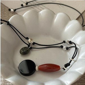 Macro detail of a handmade black braided cord necklace with vintage stones in a ceramic bowl