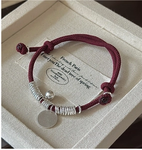 Detail of red woven rope bracelet with S925 silver charms in a jewelry gift box