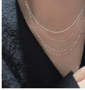 Detail view of layered S925 sterling silver necklaces on a grey textured blazer