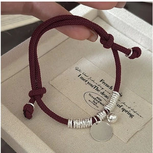 Close-up of burgundy red woven rope bracelet with silver bells and round metal tag