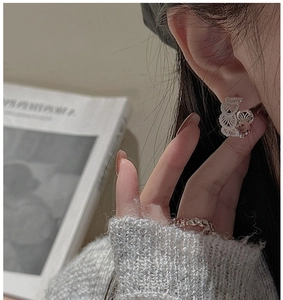 Macro shot of silver lace-textured earrings and matching wave ring on a model