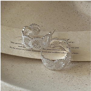 Detailed macro of C-shaped silver earrings with vintage lace texture on a neutral plate