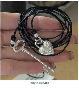 Vue macro des pendentifs clé et cadenas cœur en argent sur un cordon tressé noir