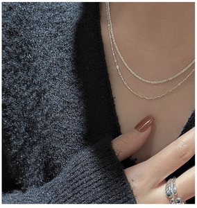 Détail d'un collier double en argent S925 et d'une bague sur un pull en tricot noir