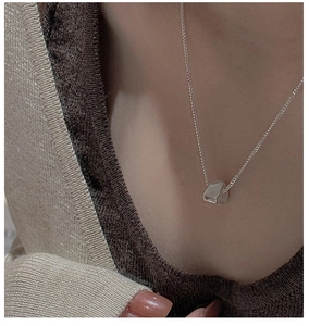 Detail of minimalist S925 sterling silver triangle necklace on a model wearing brown knitwear