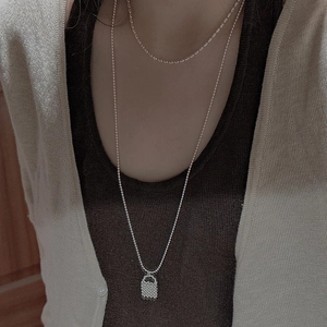 Close-up of layered S925 silver necklace with detailed woven handbag pendant design
