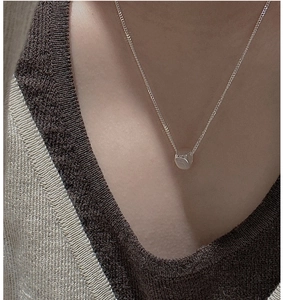 Macro shot of minimalist silver cylinder pendant on a fine chain worn on the collarbone