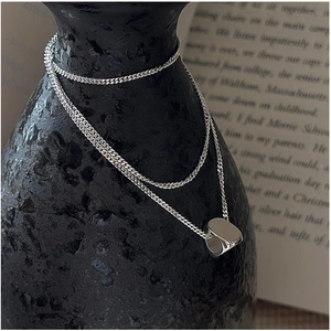 Detail view of a minimalist silver geometric pendant on a fine Cuban chain against black ceramic