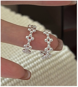Vue détaillée des créoles fleuries perlées en argent sur un fond en tricot blanc