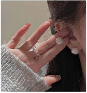 Close-up of liquid metal style wavy ring and large lustrous pearl stud earrings on model