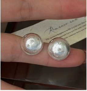 Macro shot of brushed silver star earrings with zircon stone details held by hand