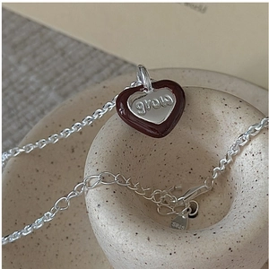 Detail of S925 silver heart necklace with brown enamel and engraved grow text
