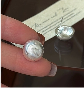 Macro shot of silver star-engraved earrings with brushed texture on a mirror surface
