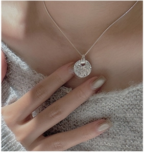 Macro shot of minimalist silver round pendant with textured lava surface on grey sweater