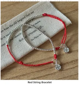 Close-up of S925 silver beaded red cord bracelets with engraved round pendants on a wooden table