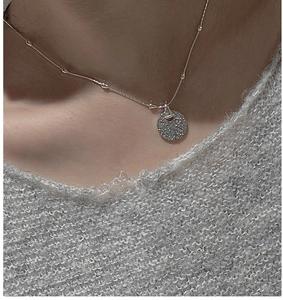Detail of S925 sterling silver necklace with textured round pendant on a grey sweater