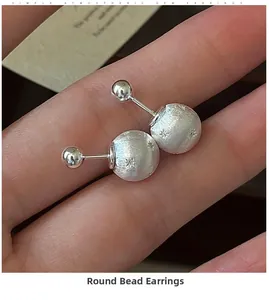 Macro detail of silver S925 star-engraved brushed ball earrings held by hand