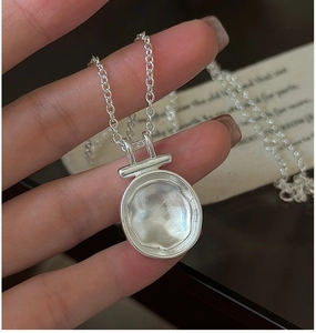 Macro shot of silver irregular textured disc pendant necklace held in hand