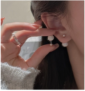 Close-up of double pearl earrings and silver heart ring worn on a person